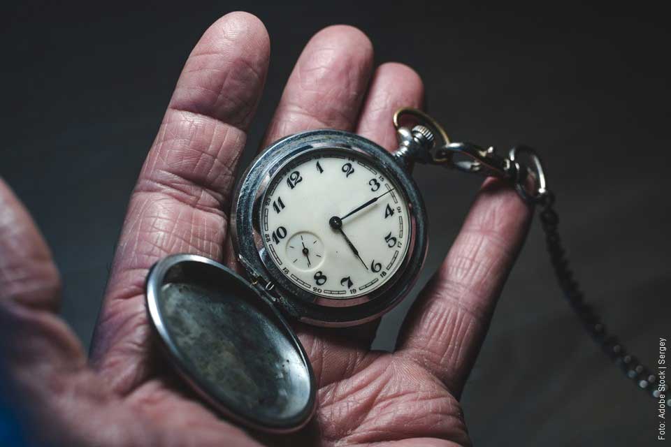 Hand eines alten Menschen hält eine Taschenuhr